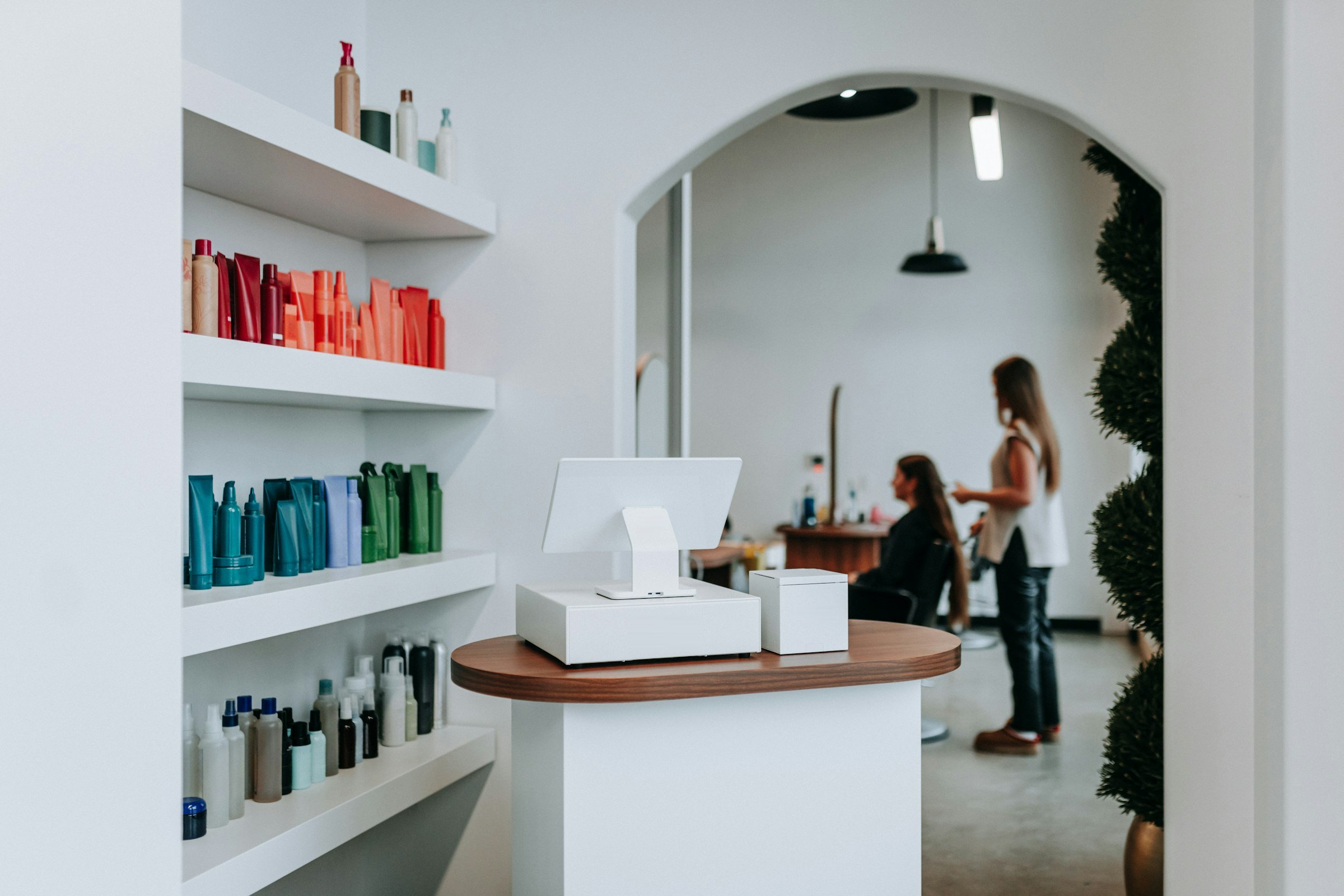 Heller Salon: leere Empfangstheke, dahinter eine Friseurin mit Kundin